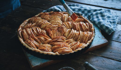 Glänzender Apfelkuchen angerichtet auf einem dunkeln Holzuntergrund. | © Getty Images / GMVozd
