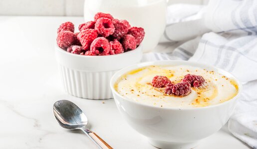 Griesbrei garniert mit Himbeeren in weißer Schüssel. | © Getty Images / Rimma_Bondarenko
