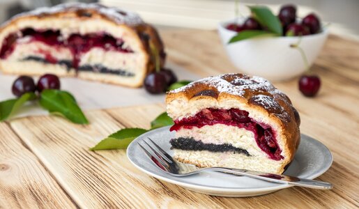 Kuchenschnitt, angeschnitten mit Füllung aus Kirschen und Mohn, angerichtet auf Holzuntergrund. | © Getty Images / Nemer-T