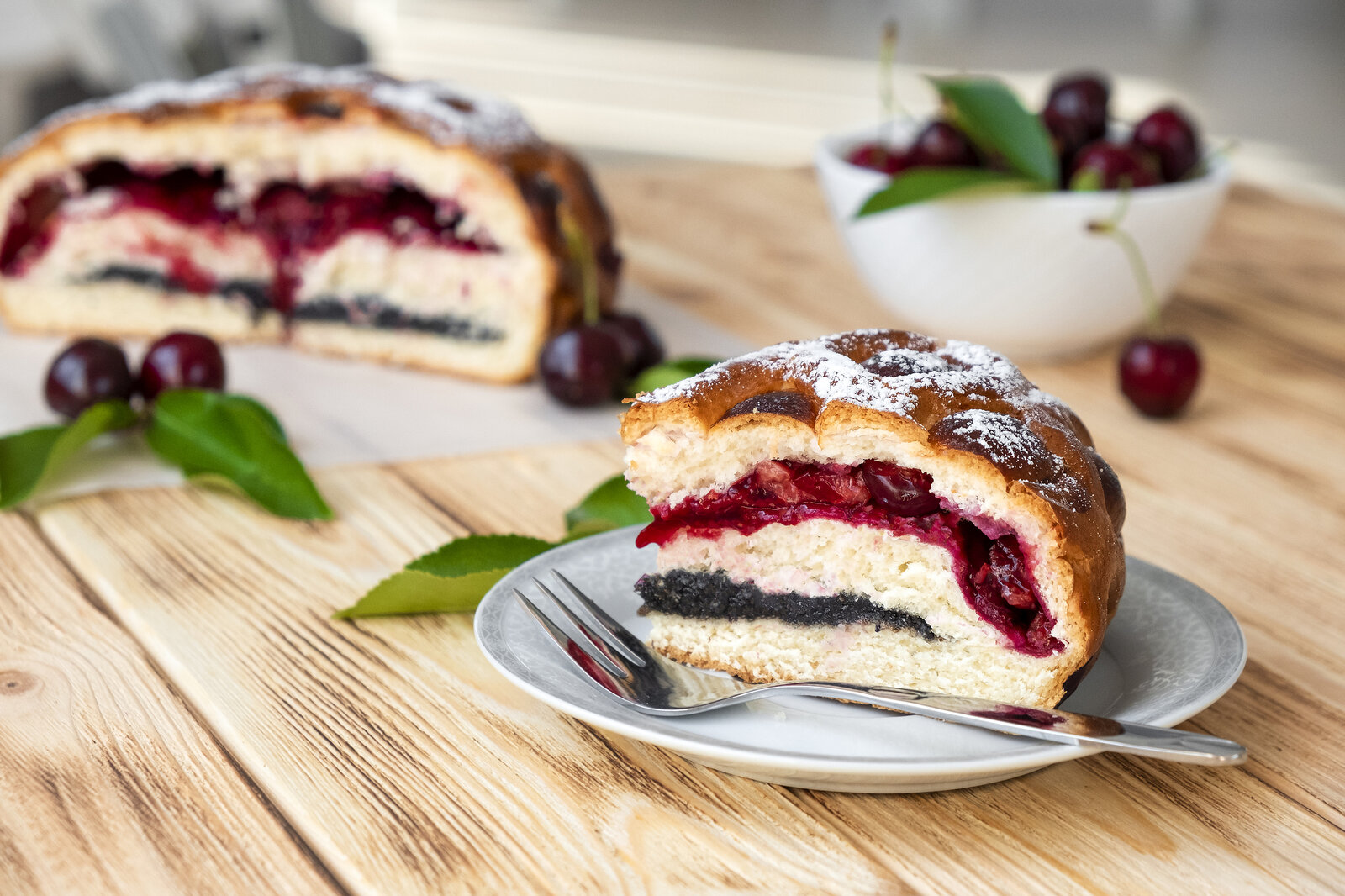 Kuchenschnitt, angeschnitten mit Füllung aus Kirschen und Mohn, angerichtet auf Holzuntergrund. | © Getty Images / Nemer-T