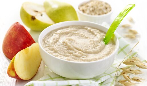 Brei in Keramikschüssel, darin ein Babylöffel, dahinter ein Apfel. | © Getty Images / 	Magone