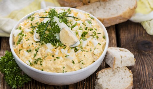 Eiersalat in weißer Schüssel, bestreut mit frischer Petersilie, daneben Brotscheiben. | © Getty Images / 	HandmadePictures