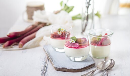 Weiße Creme geschichtet in Dessertglas, on top Rhabarberkompott. Frühlingshafte Atmosphäre und Blüten im Hintergrund. | © Getty Images / 	Westend61