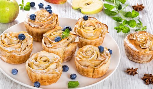 Mehrere Muffins mit Apfelscheiben garniert und frischen Blaubeeren belegt auf einem Teller angerichtet. | © Adobe Stock / myviewpoint