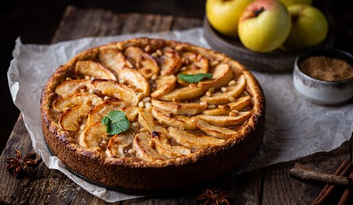 Apfelkuchen auf Holzuntergrund, daneben frischer Apfel und etwas frische Minze. | © Adobe Stock / petrrgoskov