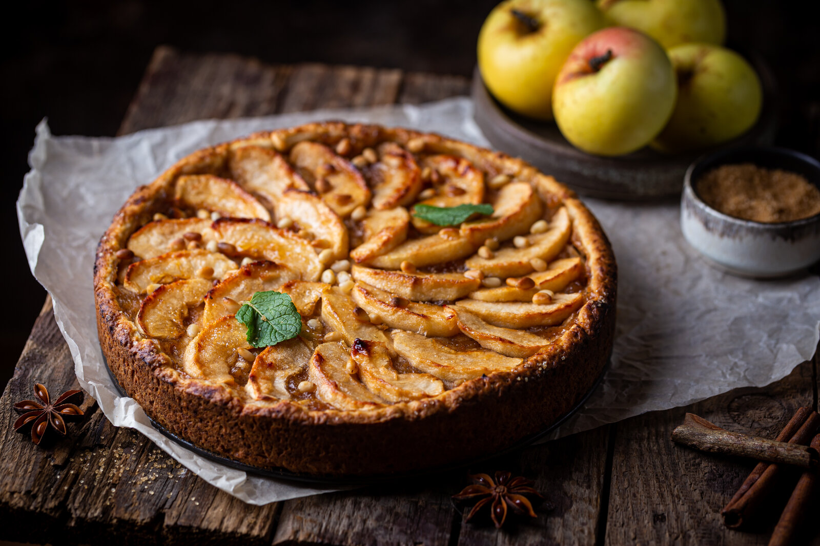 Apfelkuchen auf Holzuntergrund, daneben frischer Apfel und etwas frische Minze. | © Adobe Stock / petrrgoskov