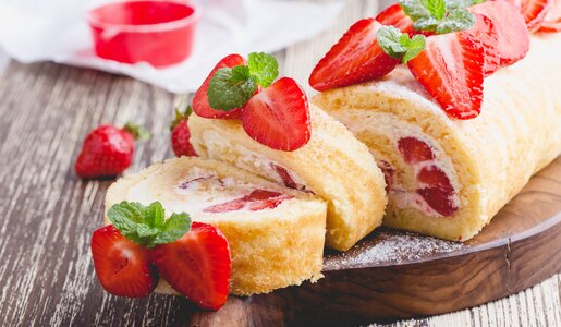 Aufgeschnittene Erdbeer-Biskuitrolle mit frischen Beeren und reichlich Puderzucker garniert. | © Getty Images / 	istetiana