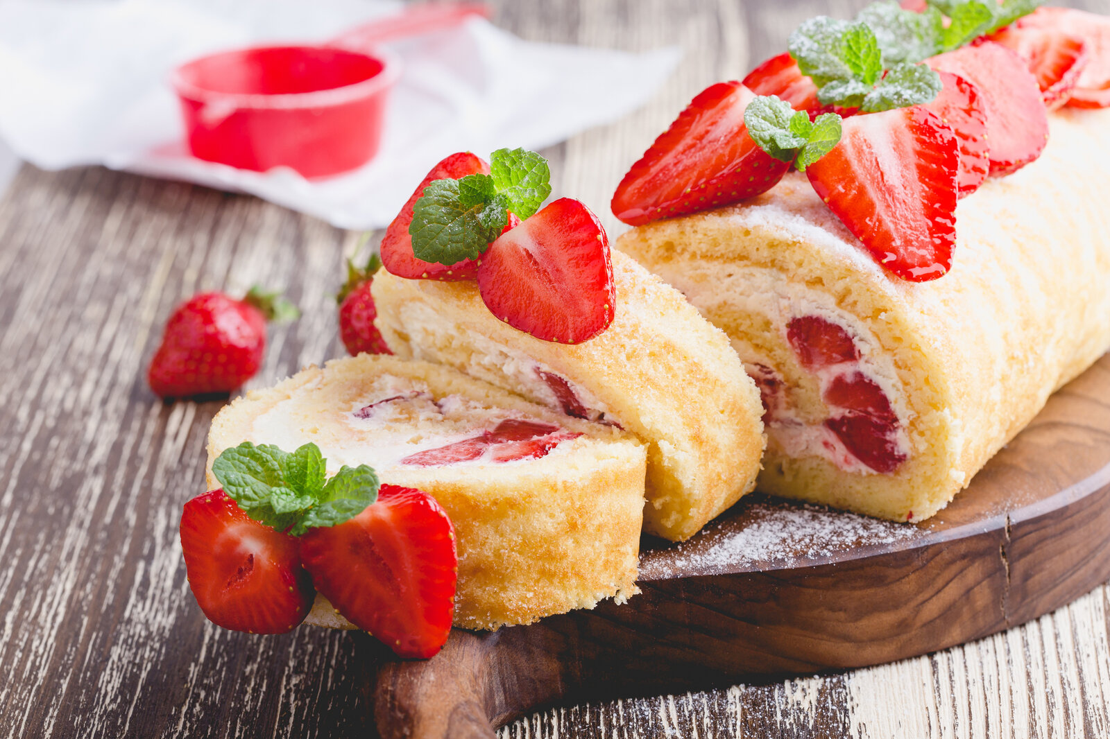Aufgeschnittene Erdbeer-Biskuitrolle mit frischen Beeren und reichlich Puderzucker garniert. | © Getty Images / 	istetiana