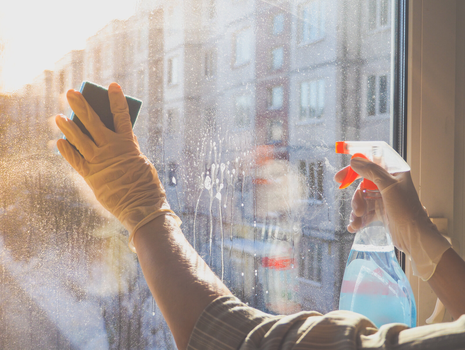Hände in gelben Gummihandschuhen putzen mit Schwamm und Reinigungsmittel ein Fenster in der Morgensonne. | © Adobe Stock/ sablinstanislav