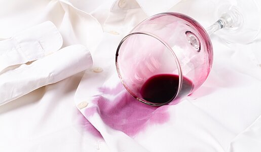 Ein umgekipptes Weinglas mit rotem Wein hat einen großen Fleck auf einem weißen Hemd hinterlassen. | © Adobe Stock/ Gala_Didebashvili