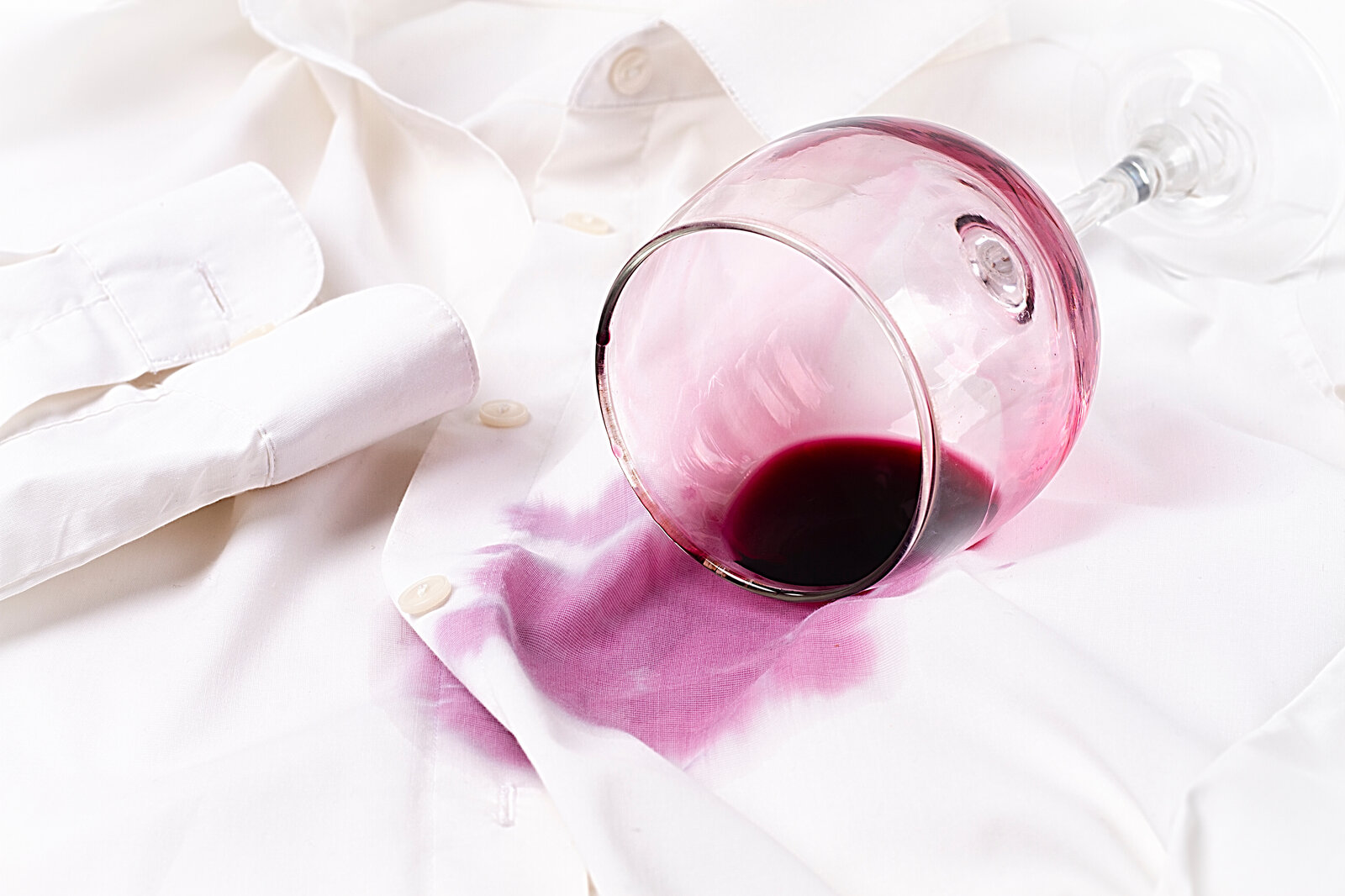 Ein umgekipptes Weinglas mit rotem Wein hat einen großen Fleck auf einem weißen Hemd hinterlassen. | © Adobe Stock/ Gala_Didebashvili