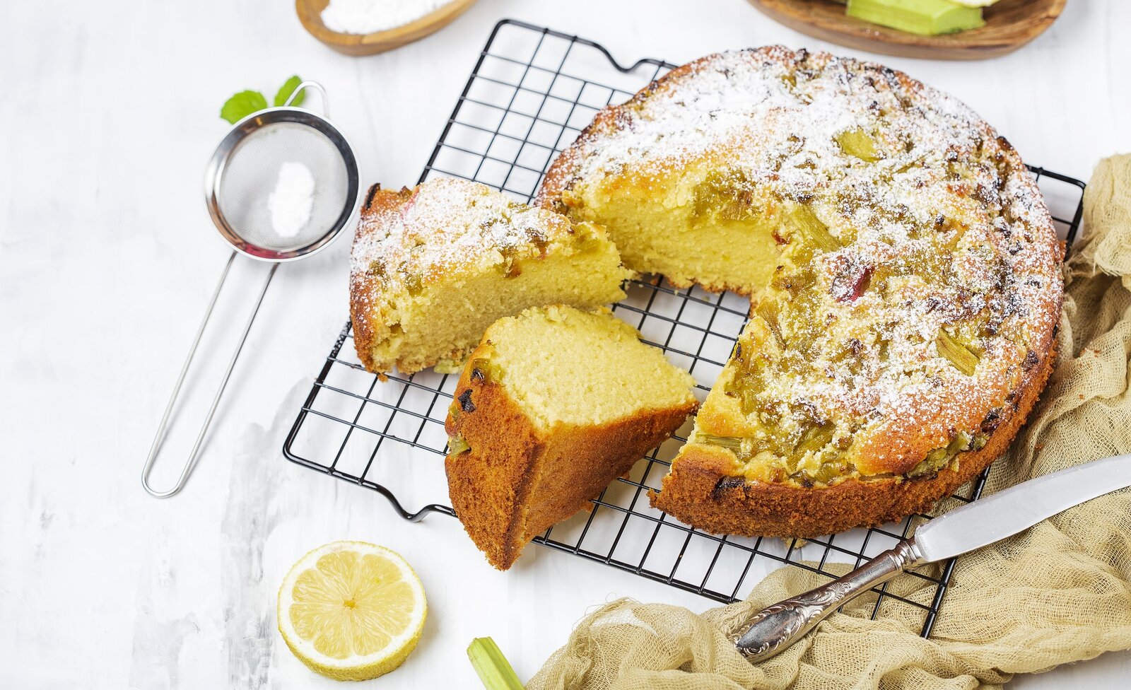 Angeschnittener Joghurtkuchen auf Küchengitter, daneben Zitronenscheiben. | © Getty Images /Pronina Marina