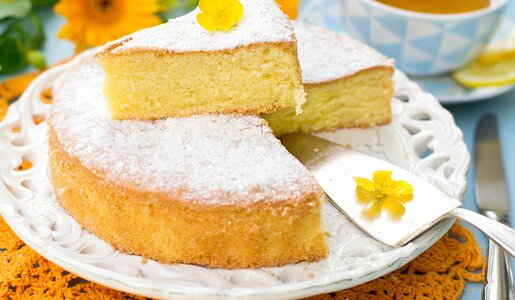 Angeschnittener Joghurtkuchen auf Kuchenplatte, bestreut mit Puderzucker und dekoriert mit gelber Blüte. | © Getty Images / larik_malasha