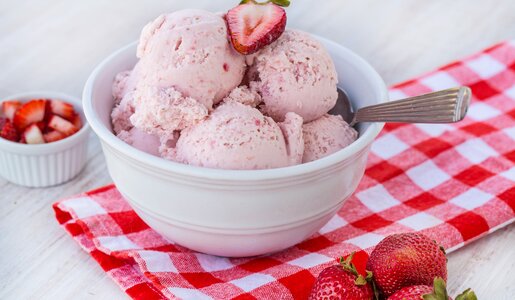 Drei Erdbeereis-Kugeln in einer weißen Schüssel angerichtet, daneben frische Minze und frische Erdbeeren. | © Getty Images / 	carolmellema