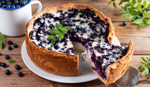 Angeschnittener Blaubeerkuchen, daneben frische Blaubeeren und Kräuter. | © Getty Images / Qwart