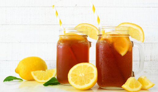 Zwei Zitroneneistee in Gläsern, jeweils ein gestreifter Strohhalm im Tee und daneben frische Zitronen. | © Getty Images / jenifoto