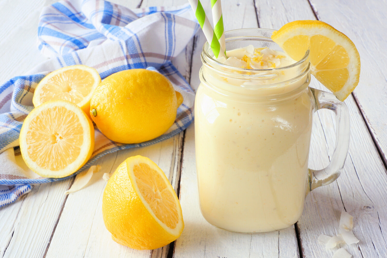 Zitronen-Joghurt-Smoothie im Glas, darin ein Strohhalm und daneben frische Zitronen. | © Getty Images / jenifoto