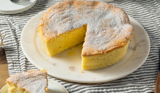 Angeschnittener Quarkkuchen auf einem weißen Kuchenteller auf einem Holztisch. | © Getty Images / 	bhofack2