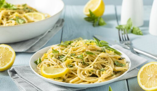 Spaghetti mit Basilikum und Zitrone auf Pastateller, daneben frische Zitronenscheiben und Basilikumblätter. | © Getty Images / 	bhofack2
