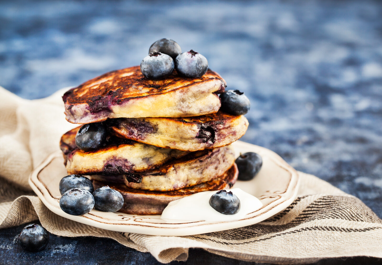 Fluffige Blaubeer-Pfannkuchen gestapelt auf einem Teller, der auf einem Leinentuch steht. | © Adobe Stock / kate_smirnova