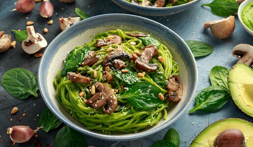 Spinat-pasta auf einem Teller angerichtet, daneben aufgeschnittene Avocado und frischer Babyspinat. | © Adobe Stock / Nick van Bree