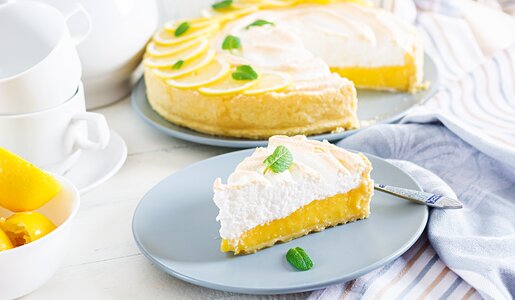 Angeschnittener Quarkkuchen mit Zitronenmousse, dekoriert mit frischen Zitronenscheiben. | © Adobe Stock / timolina