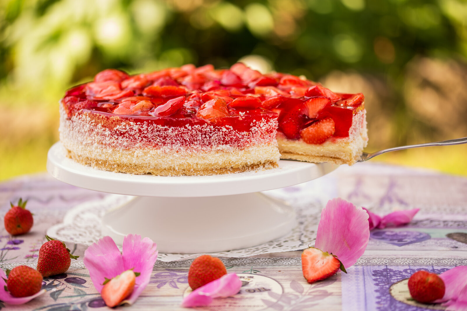 Eisgekühlter Joghurtkuchen mit Erdbeeren in sommerlicher Umgebung auf Tortenboden. | © Adobe Stock / cstirit