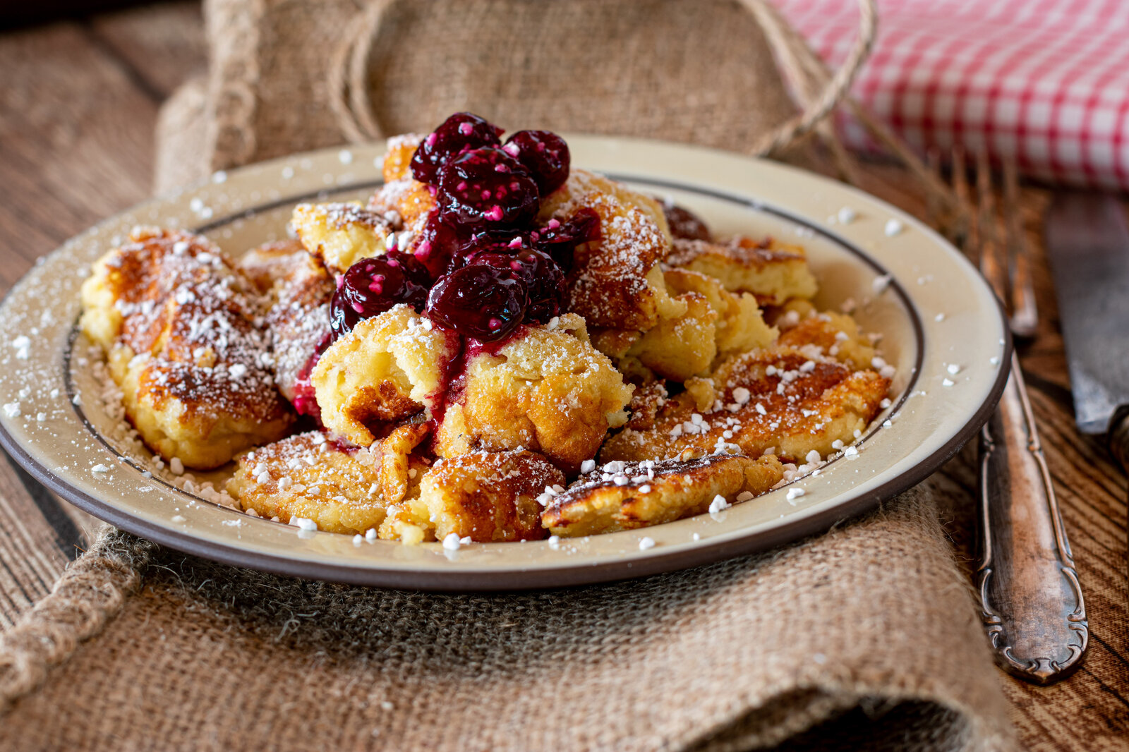 Fluffiger Kaiserschmarrn Low Carb ohne Zucker mit Puderzucker bestreut und mit heißen Kirschen garniert. | © Adobe Stock / Angelika Heine