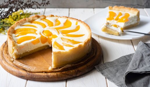 Angeschnittener Joghurtkuchen mit Pfirsich, auf einem Teller angerichtet, dahinter das Stück Kuchen auf einem anderen Teller. | © Adobe Stock /  Светлана Терлюкевич