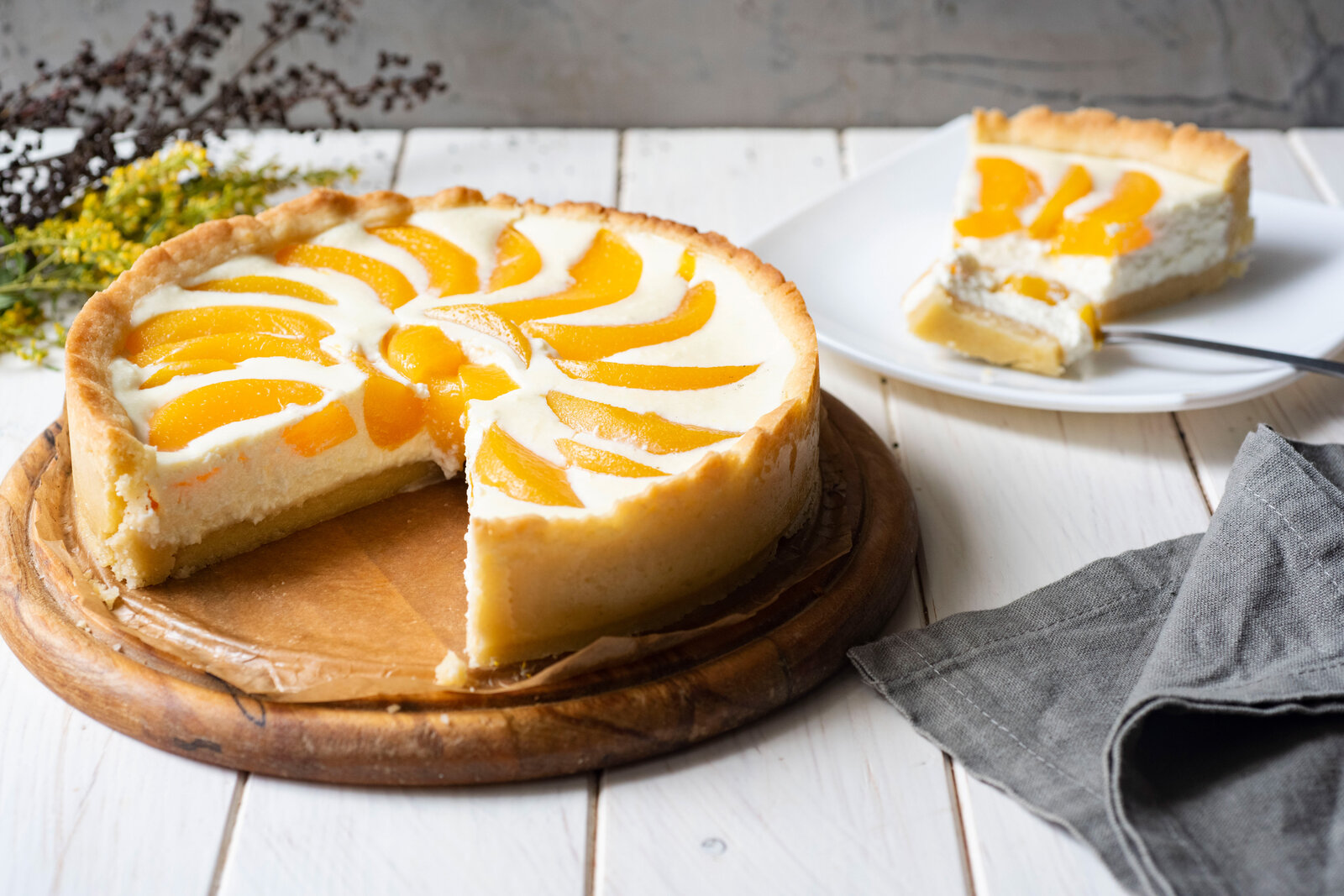 Angeschnittener Joghurtkuchen mit Pfirsich, auf einem Teller angerichtet, dahinter das Stück Kuchen auf einem anderen Teller. | © Adobe Stock /  Светлана Терлюкевич