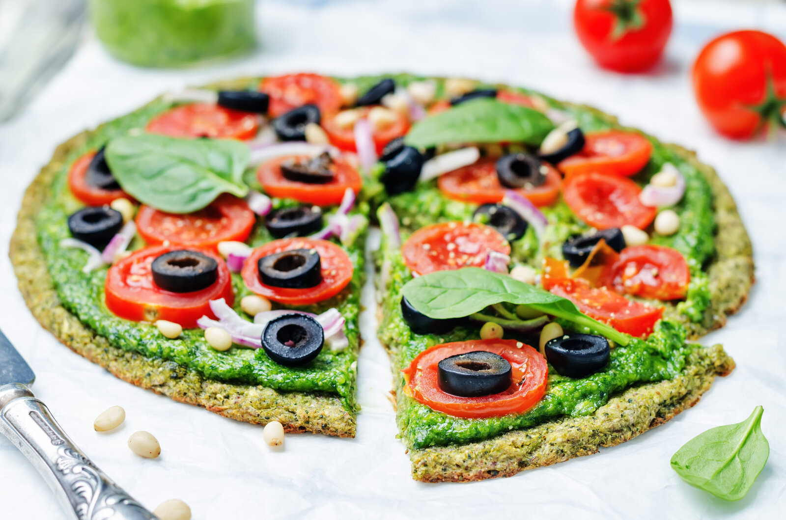 Angeschnittene Low Carb Zucchini-Pizza ohne Mehl, belegt mit Oliven, Tomaten, Basilikum und Pinienkerne. | © Adobe Stock / nata_vkusidey