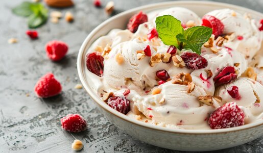Mehrere Kugeln Himbeereis, getoppt mit Nüssen in einer weißen Schale, daneben viele weitere frische Himbeeren. | © Adobe Stock / Leo