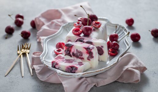 Angeschnittenes Kirsch-Joghurt-Parfait ohne Zucker mit frischen Kirschen auf einem weißen Teller angerichtet. | © Getty Images / 	yumehana