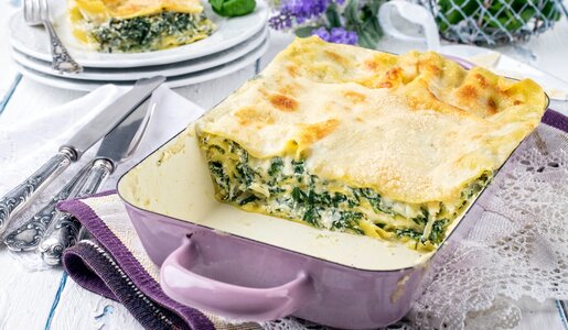 Low Carb Spinat-Lasagne in einer lila-Auflaufform, angeschnitten und dahinter auf einem Teller ein weiteres Stück Lasagne. | © Adobe Stock / HLPhoto