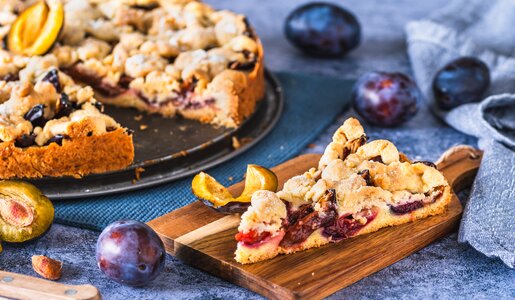 Angeschnittener Pflaumenkuchen auf einem Kuchenteller, im Vordergrund ein Stück des Kuchens auf einem weiteren Teller. | © Getty Images / Daniela Baumann