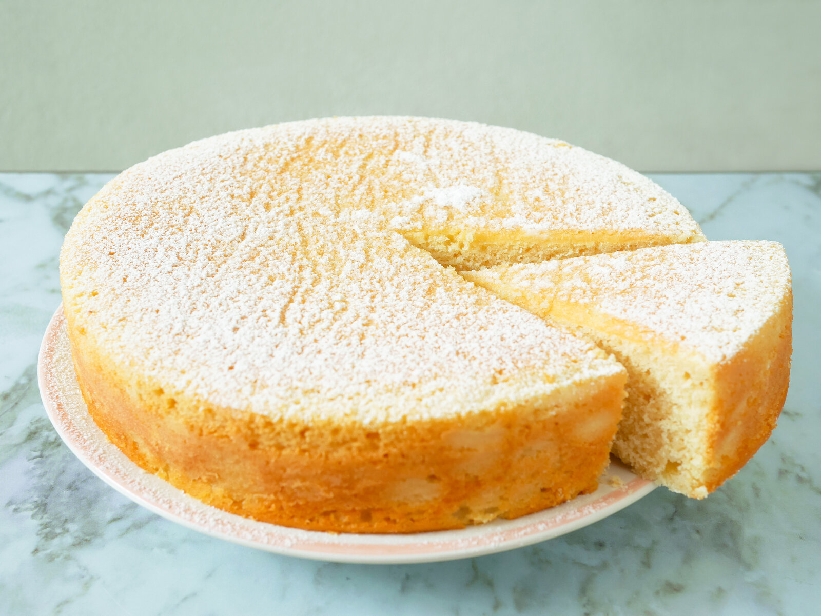Angeschnittener Joghurtkuchen auf einem Kuchenteller mit Puderzucker. | © Getty Images / p_saranya