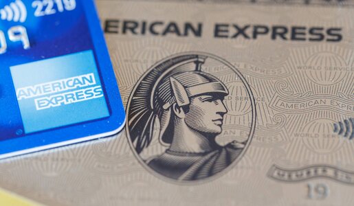 Ausschnitt einer blauen American Express-Karte, die auf einer platinfarbenen Karte mit dem markanten Centurion-Kopf liegt. | © IMAGO/Zoonar