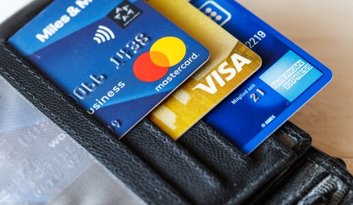 Drei Kreditkarten (Mastercard, Visa und American Express) stecken in einem schwarzen Lederetui auf hellem Hintergrund. | © IMAGO/Panthermedia