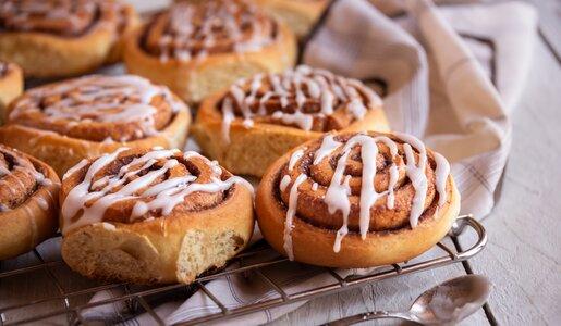 Mehrere Zimtschnecken auf einem Kuchengitter mit Zuckerguss bezogen. | © Adobe stock / Maresol