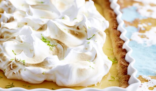 Limetten-Tarte nah, in weißer Backform mit Baiserhaube, auf bunter Tischdecke. | © 	Isabell Triemer