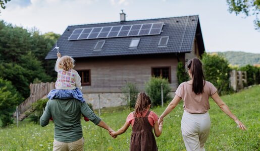 Familie steht vor einem Haus mit einer Photovoltaikanlage auf dem Dach | © Getty Images/Halfpoint Images