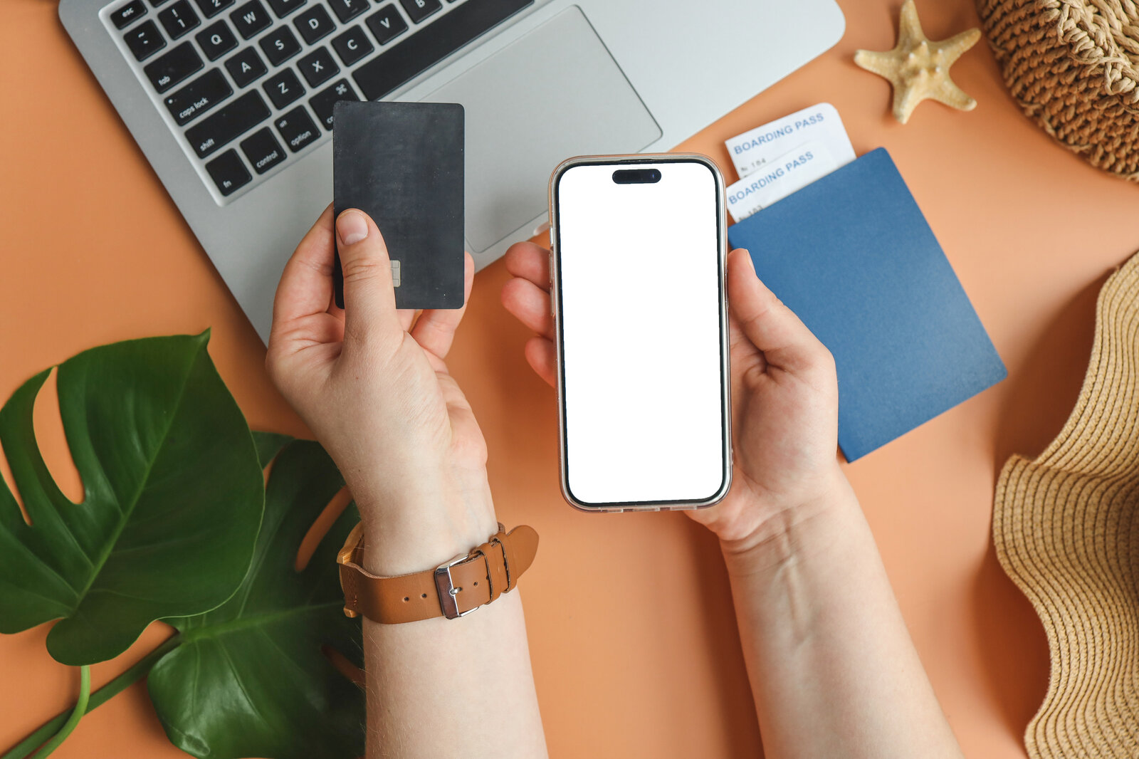 Zwei Hände halten ein Smartphone und eine schwarze Kreditkarte vor einem Laptop mit Reisepass und Boardingpässen. | © Getty Images/Bohdan Bevz